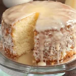 Pina Colada Pound Cake 4 Pina Colada Pound Cake topped with pineapple glaze and toasted coconut on a white cake stand.