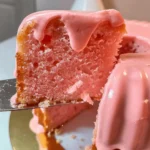 A moist strawberry buttermilk pound cake topped with pink strawberry glaze and fresh strawberries on a rustic plate.